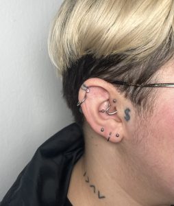 Piercing în ureche cu mai multe bijuterii, tatuaje discrete și coafură modernă, la salonul OLD INK TATTOO din București, specializat în tatuaje și piercinguri unice.